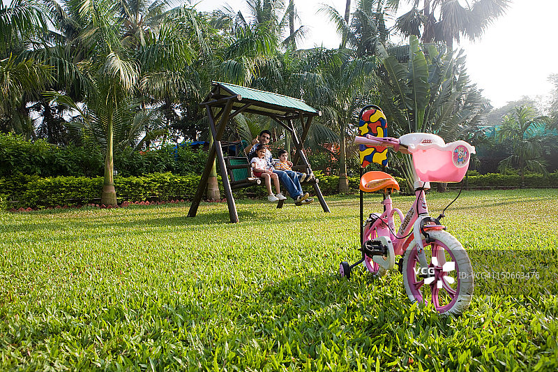 父亲和两个孩子在花园的秋千上图片素材