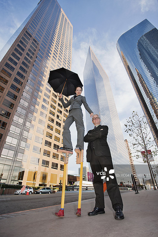 城市环境中踩着高跷的白人女商人与同事站在一起图片素材