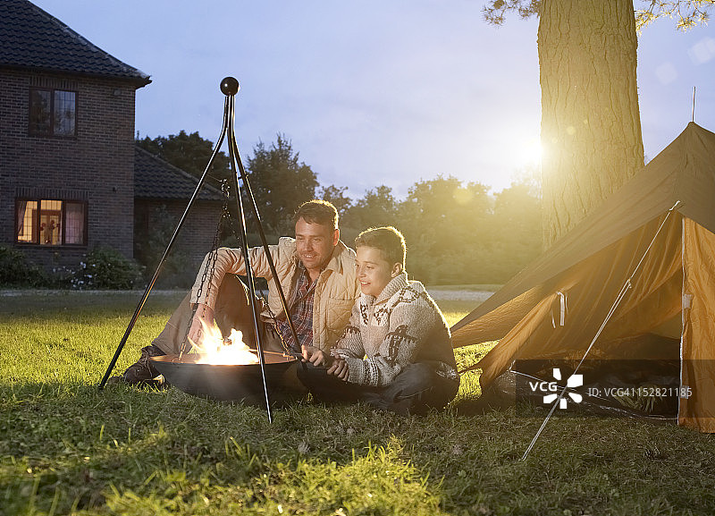 父子坐在帐篷外的篝火旁图片素材