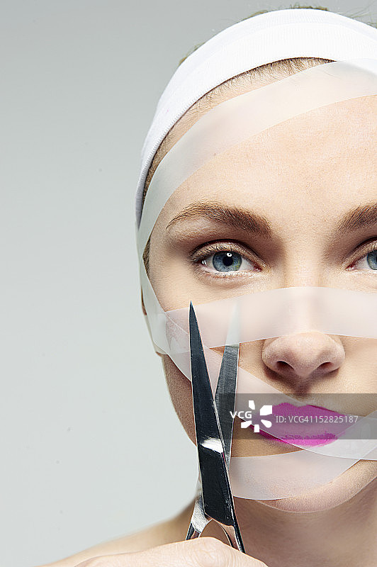 女人用剪刀剪掉脸上的胶带图片素材