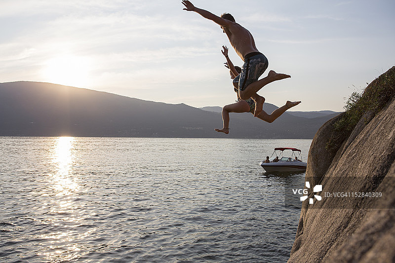 青少年从悬崖跳入湖中，下方有船图片素材