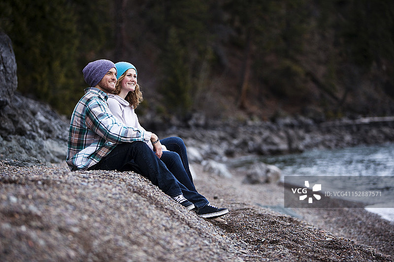 一对年轻夫妇在爱达荷州湖边的岩石海滩上欢笑图片素材