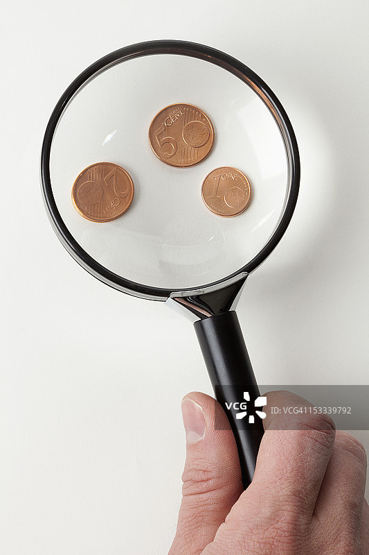男人用放大镜观察三枚铜制欧元硬币，手部特写图片素材