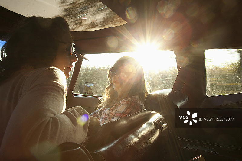 坐在老式汽车前座的两位宁静的摇滚风格女性图片素材