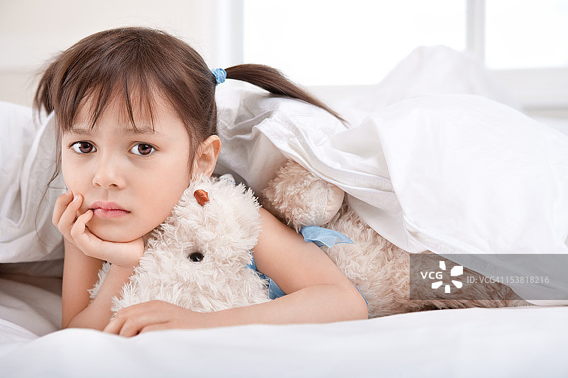 躺在毯子下，抱着泰迪熊的悲伤小女孩图片素材