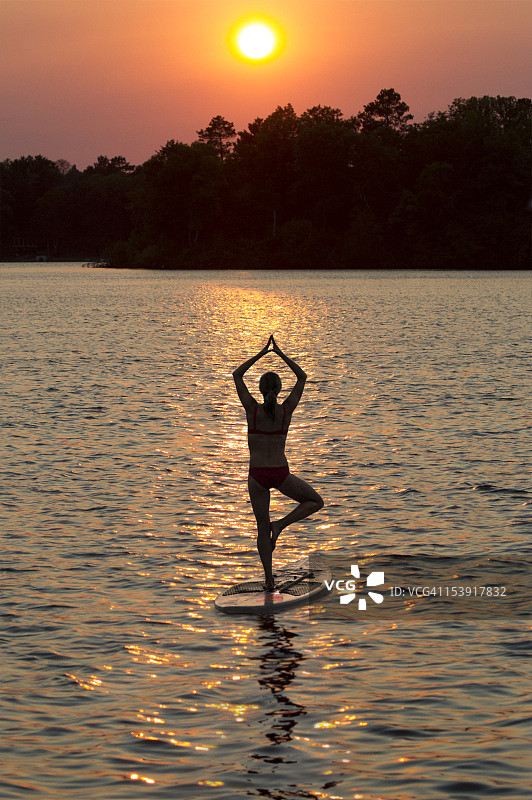 女士在日落时分在桨板上做瑜伽图片素材