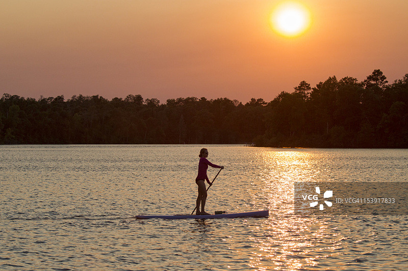 日落时分，一位女士在桨板上图片素材