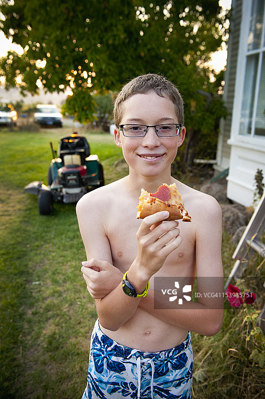 夏日午后，男孩在前院草坪上吃披萨图片素材