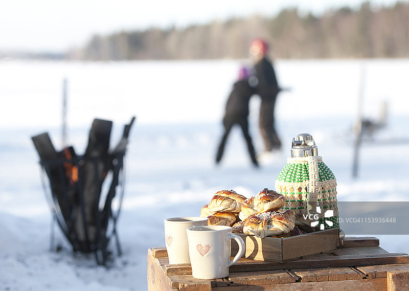 保温瓶、甜面包和马克杯摆台，背景有人图片素材