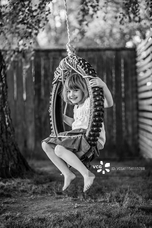 穿着朴素的在轮胎秋千上的黑白少女图片素材