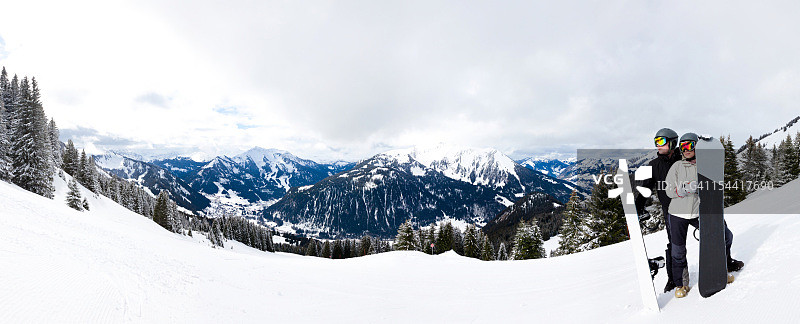 两名滑雪者眺望多云的山脉全景图片素材