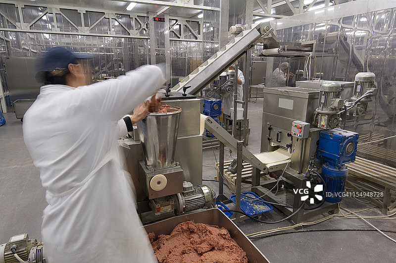 一个男人在工厂里把肉放进研磨机里图片素材