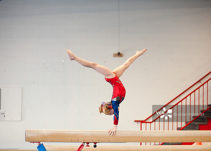 年轻的体操运动员在平衡木上手倒立劈叉图片素材