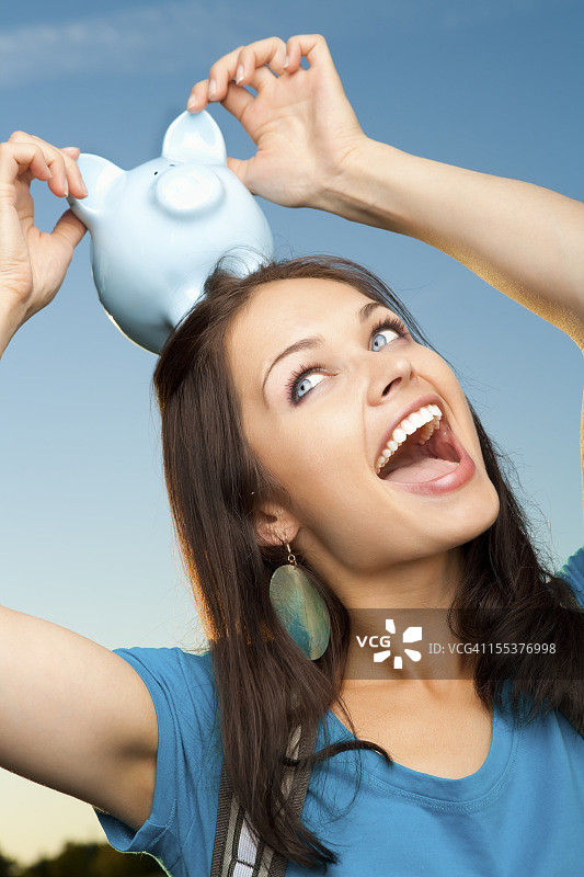 微笑的大学生拿着蓝色小猪存钱罐图片素材