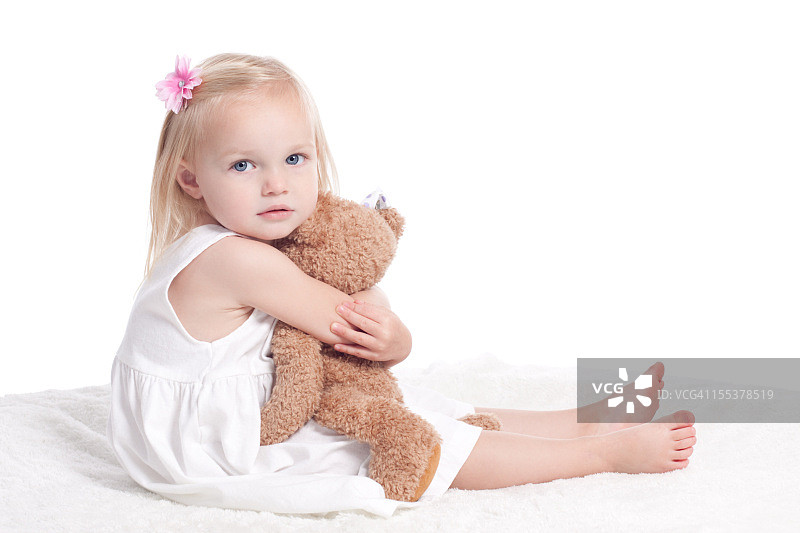 穿着白色连衣裙的悲伤小女孩抱着毛绒玩具图片素材