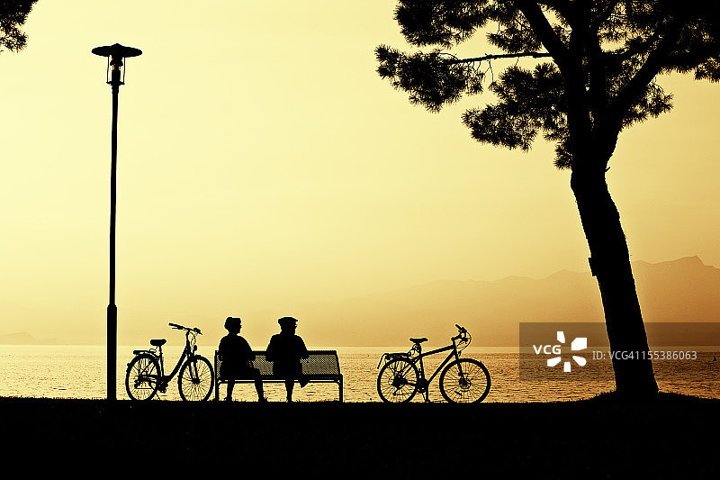 中年自行车手在日落时分的海边长椅上图片素材