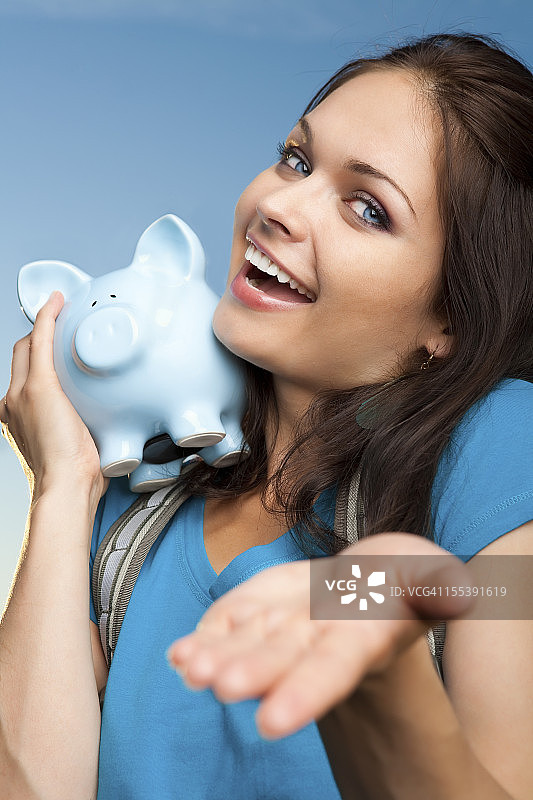 微笑的大学生拿着蓝色小猪存钱罐图片素材