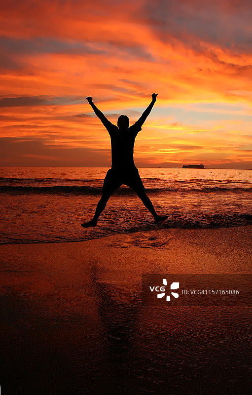 男子在日落时分的海滩上高兴地跳跃图片素材