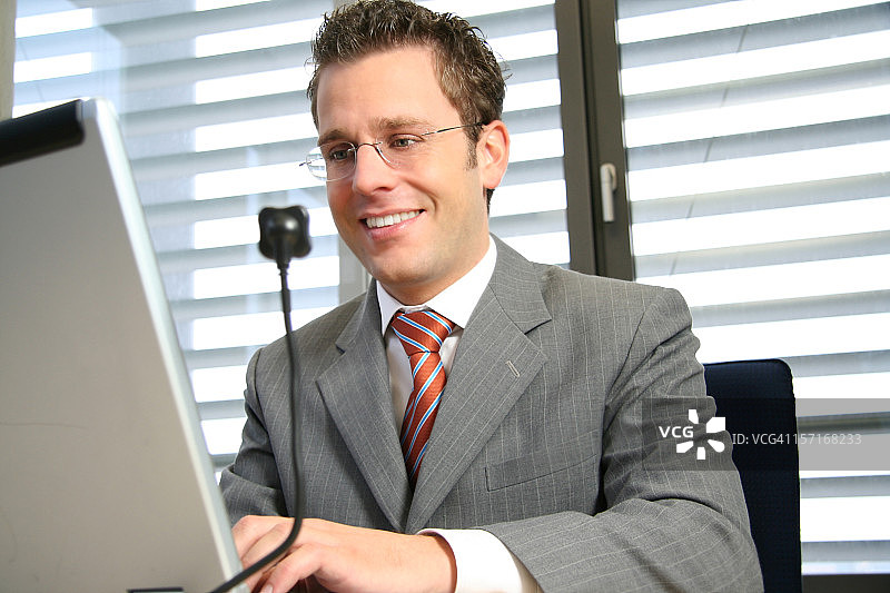 戴着眼镜，穿着灰色西装进行视频通话的微笑男人图片素材