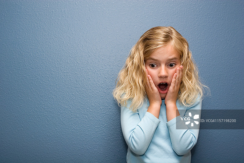 在蓝色背景下，表情害怕的可爱小女孩图片素材
