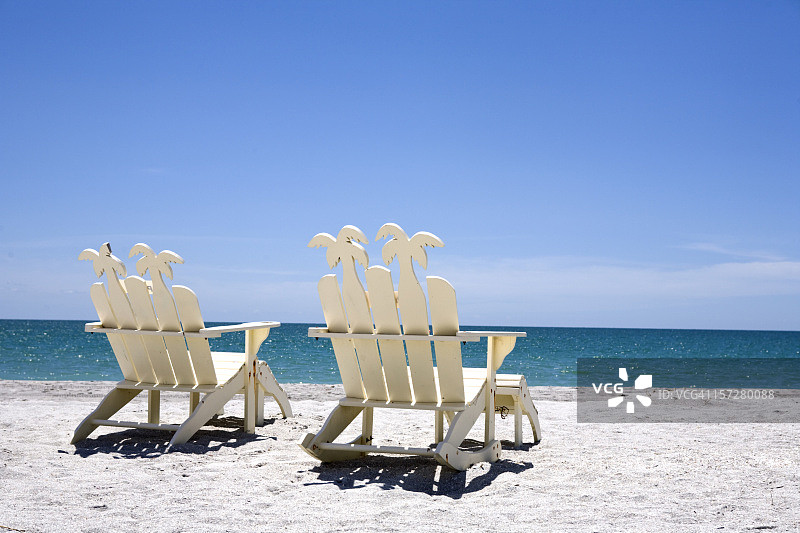 沙滩上两把白色木椅的背面，面朝大海图片素材