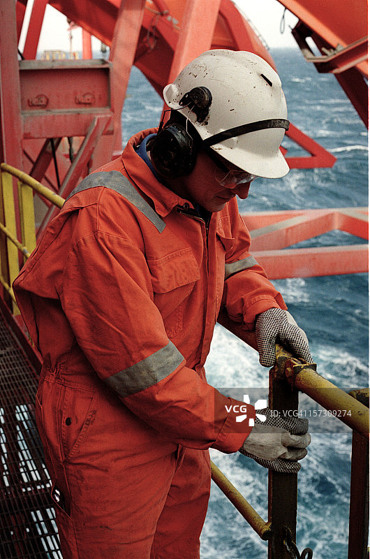 穿着橙色制服，戴着白色头盔在石油钻井平台上工作的男人图片素材