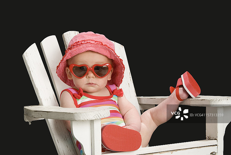 戴着太阳镜、跷着腿，在阿迪朗达克椅上放松的幼儿女孩图片素材