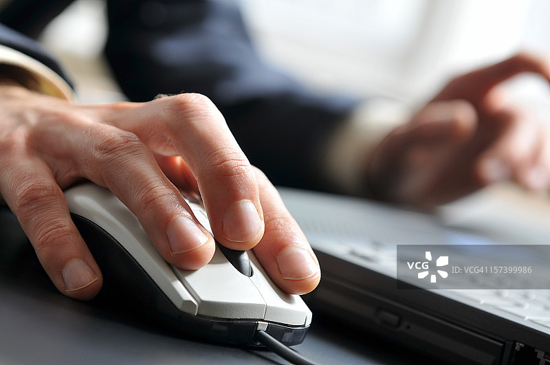 男子手握鼠标在笔记本电脑上工作特写图片素材