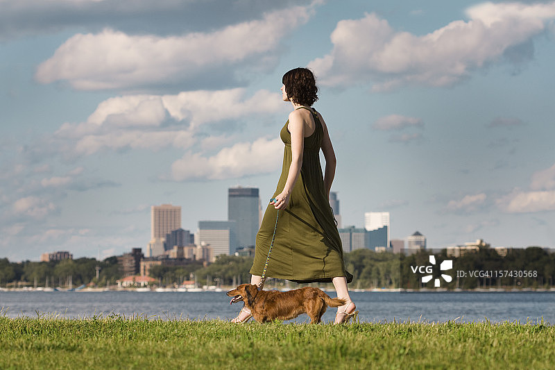 年轻女子在明尼阿波利斯卡尔霍恩湖城市公园遛腊肠犬图片素材