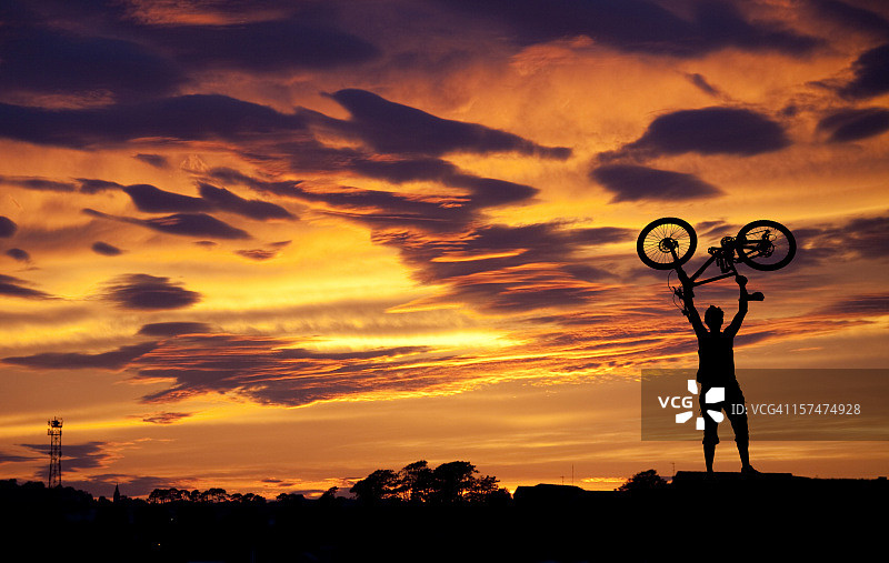 日落时分举起自行车的男子剪影图片素材