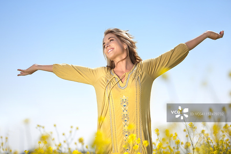 身穿黄色上衣的女人在黄色花田里张开双臂图片素材