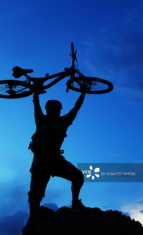 暮色蓝天下的山地自行车骑手剪影（头顶举着自行车）图片素材