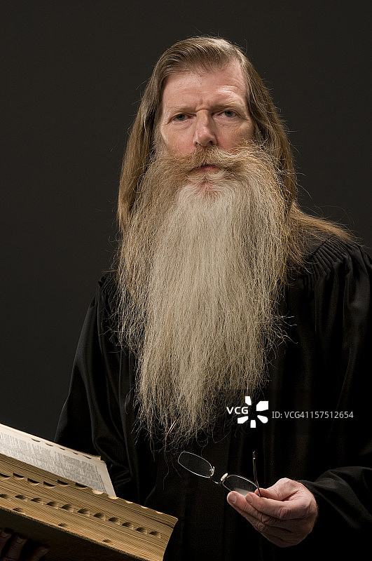 留着胡子的男人穿着学者长袍，拿着书/圣经看着镜头图片素材