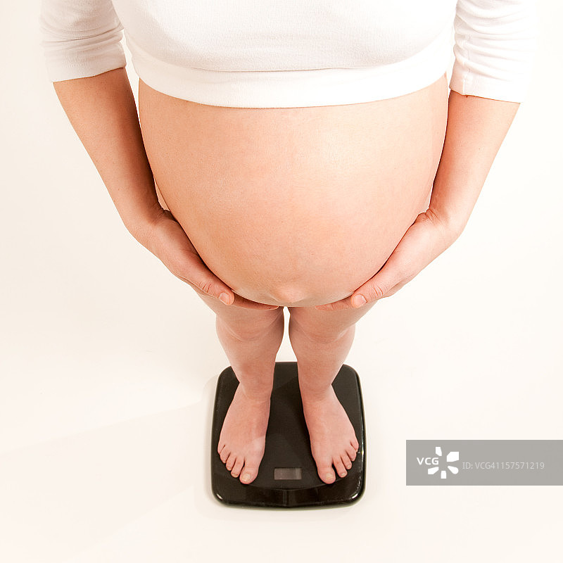 在体重秤上展示裸露腹部的孕妇图片素材