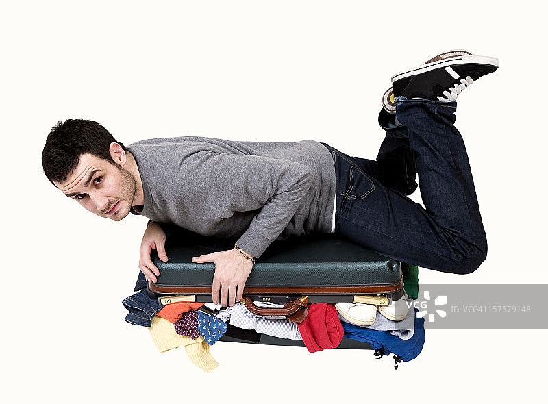 幽默的男人试图合上塞满的行李箱图片素材