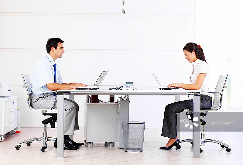 办公室里，两名商人用笔记本电脑打字图片素材