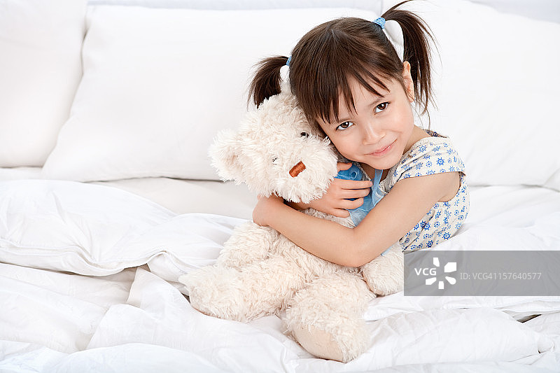 快乐的小女孩在床上抱着泰迪熊图片素材