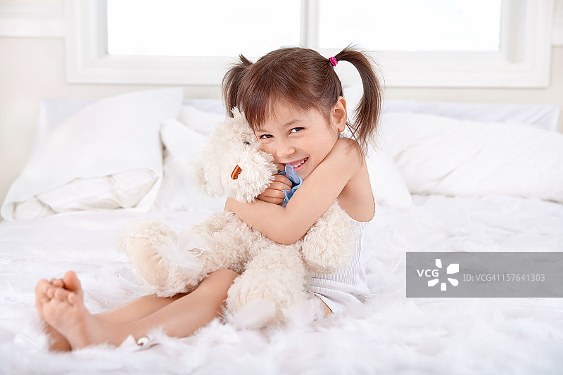 快乐的小女孩在床上抱着泰迪熊图片素材
