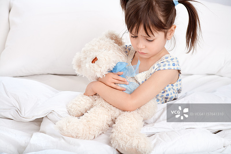 悲伤的小女孩在床上抱着泰迪熊图片素材
