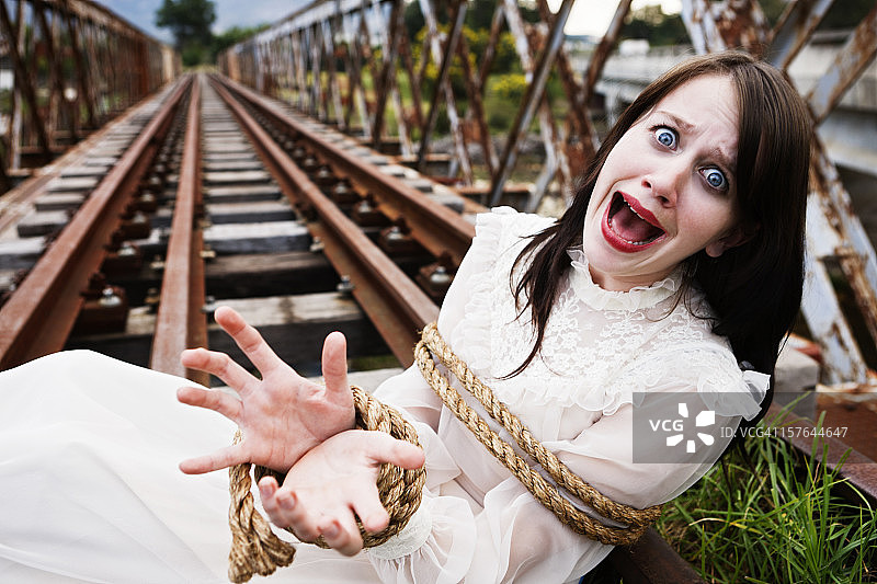 穿着维多利亚时代服装的漂亮女孩被绑在铁轨上。高潮迭起！图片素材