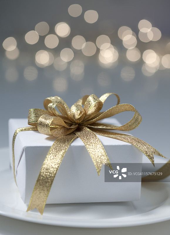 带金色丝带和蝴蝶结的白色礼品盒与模糊的灯光图片素材