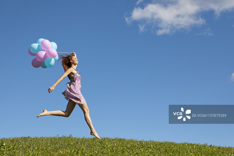 快乐的女人在草地上跳跃，拿着气球图片素材
