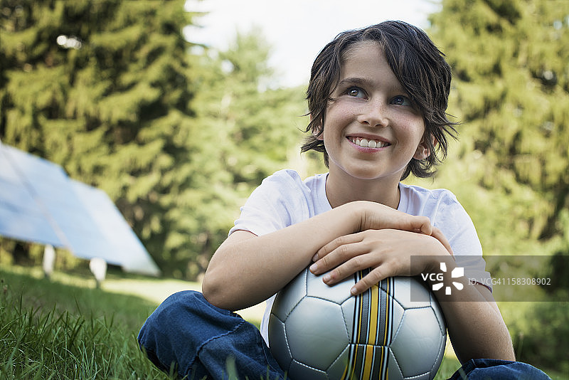 拿着足球坐在草地上的男孩，背景是太阳能电池板图片素材