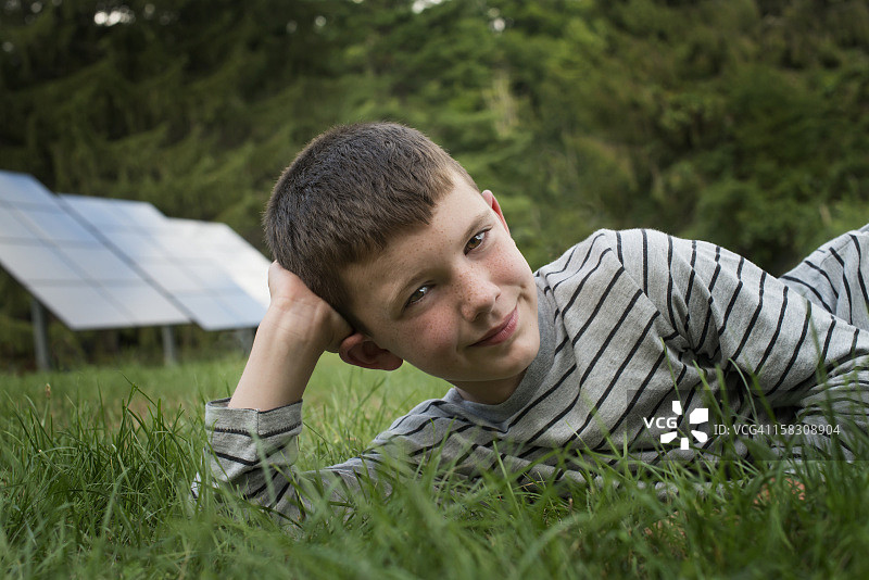 男孩躺在草地上，太阳能电池板旁边图片素材