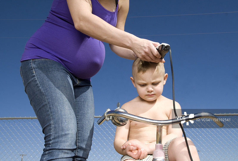 怀孕的母亲给儿子剃头图片素材