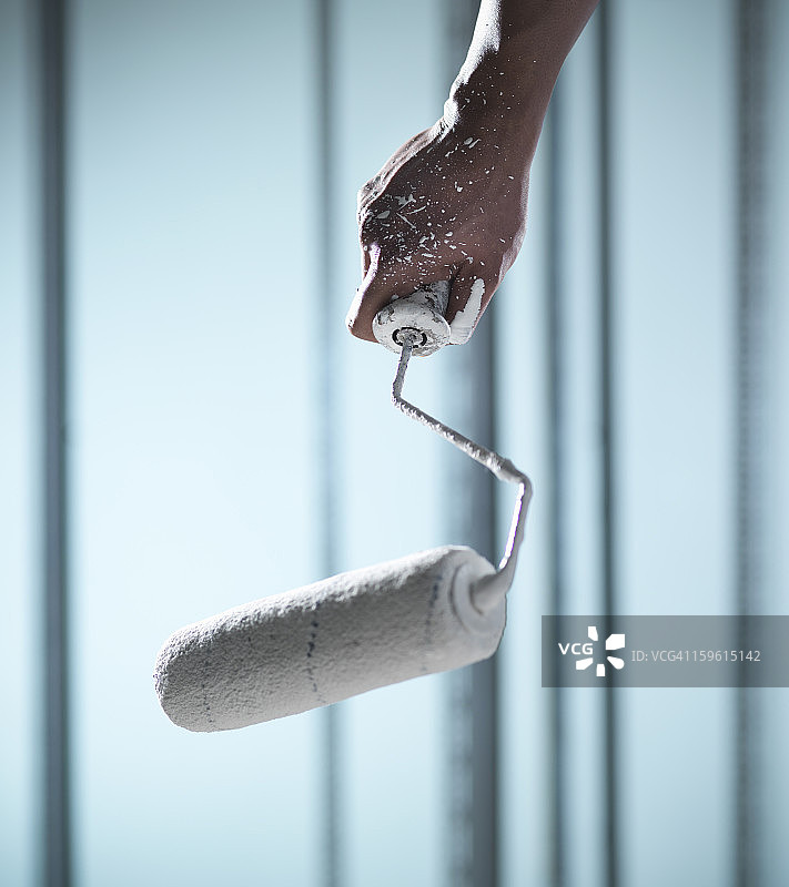 男人拿着油漆滚筒，手上溅有白色油漆图片素材