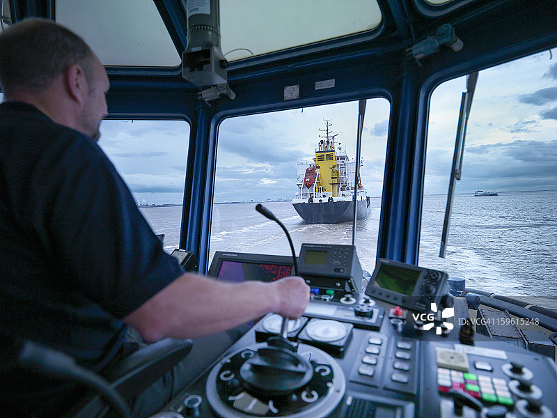 在海上驾驶拖船的船长：透过窗户看到的船舶驾驶台和拖船图片素材
