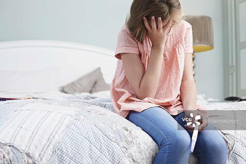 少女坐在床上，手持验孕棒图片素材
