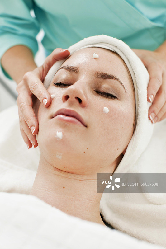 按摩师在水疗中心为年轻女子做面部按摩图片素材