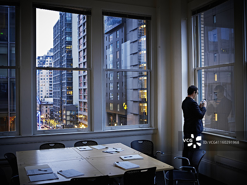 在办公室靠窗使用智能手机工作的商人图片素材